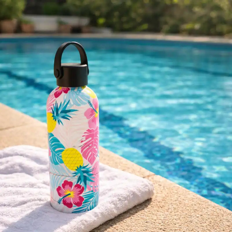 Colorful floral-patterned water bottle on a towel by a pool