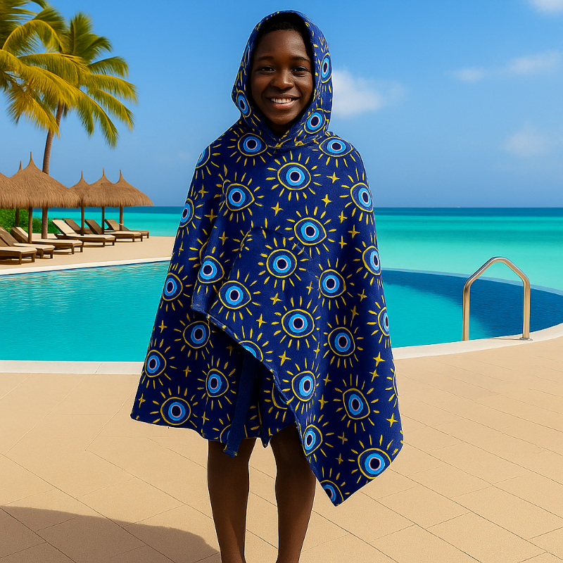 Person wearing a blue patterned hooded towel by a pool with palm trees and ocean in the background