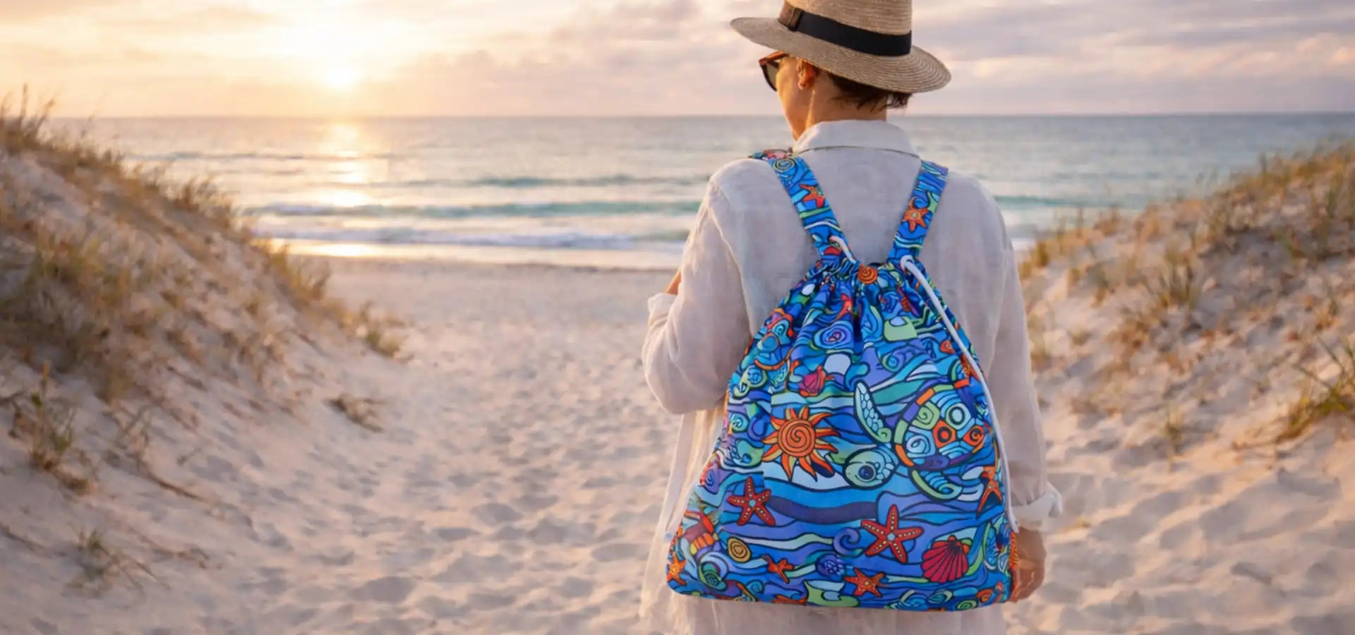 Person carrying an Ocean Oasis turtle print TowelTote on a beach at sunset