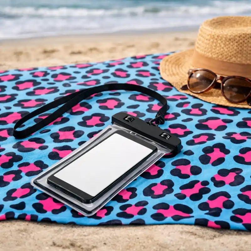 Phone case with lanyard on a leopard print towel with sunglasses and hat on a beach.