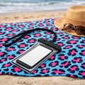 Phone case with lanyard on a leopard print towel with sunglasses and hat on a beach.