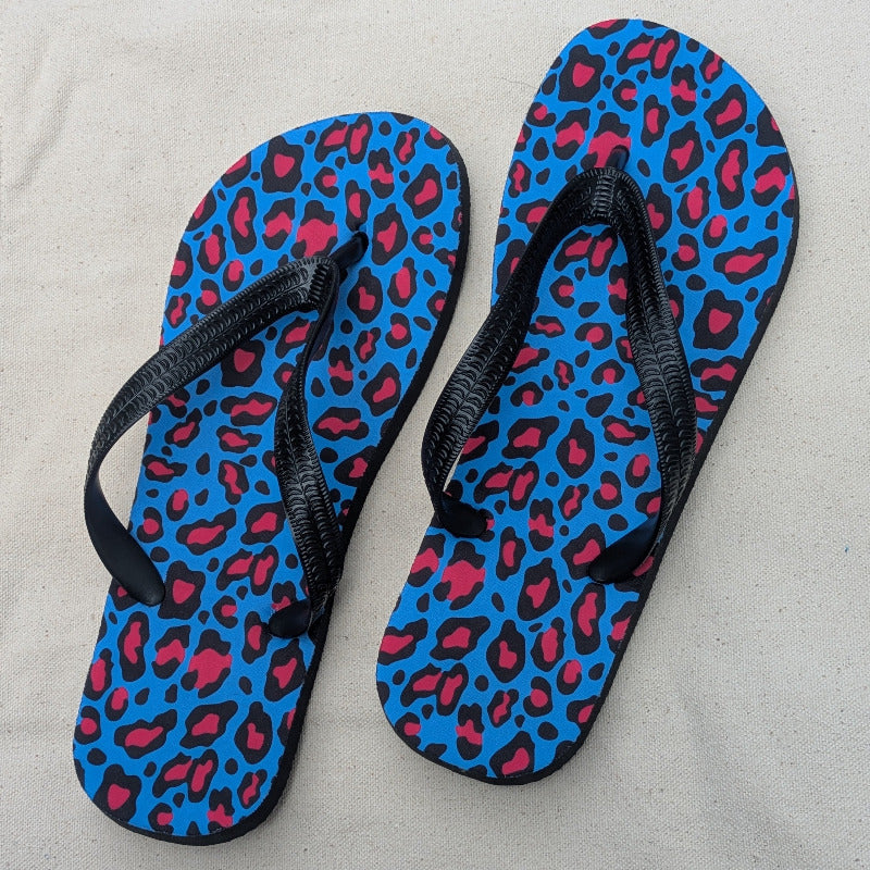 Blue flip-flops with pink leopard print and black straps on a cream background